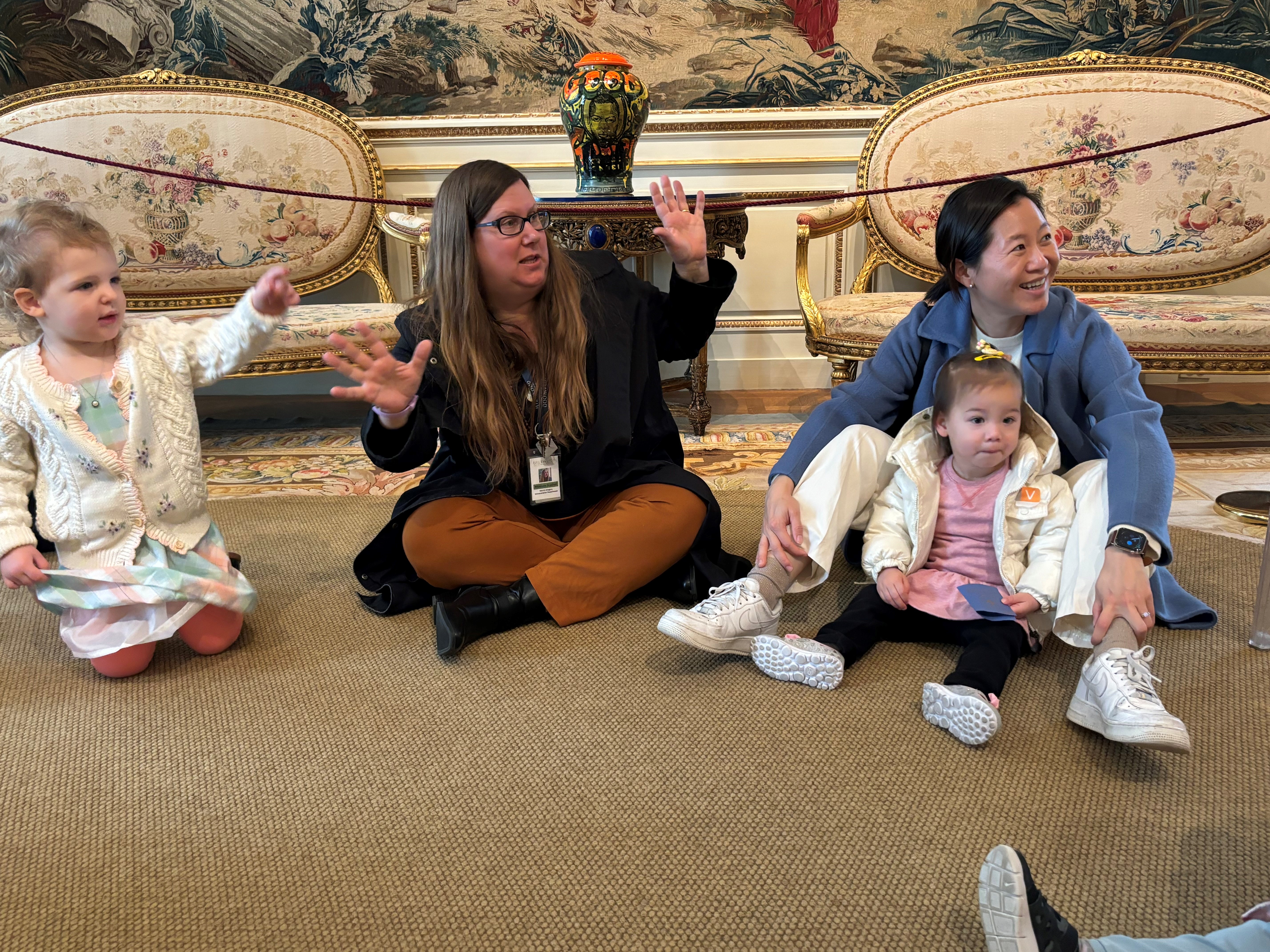 a teacher, preschool students, and a parent, gesture and point excitedly at art in the mansion