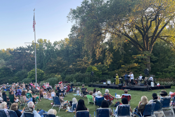 Image of visitors gathered on a large, grassy area watching a jazz concert.