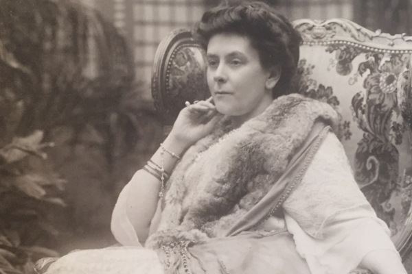 Image of a photographic portrait of Olga Paley. She sits in a chair with her head resting on her hand. 