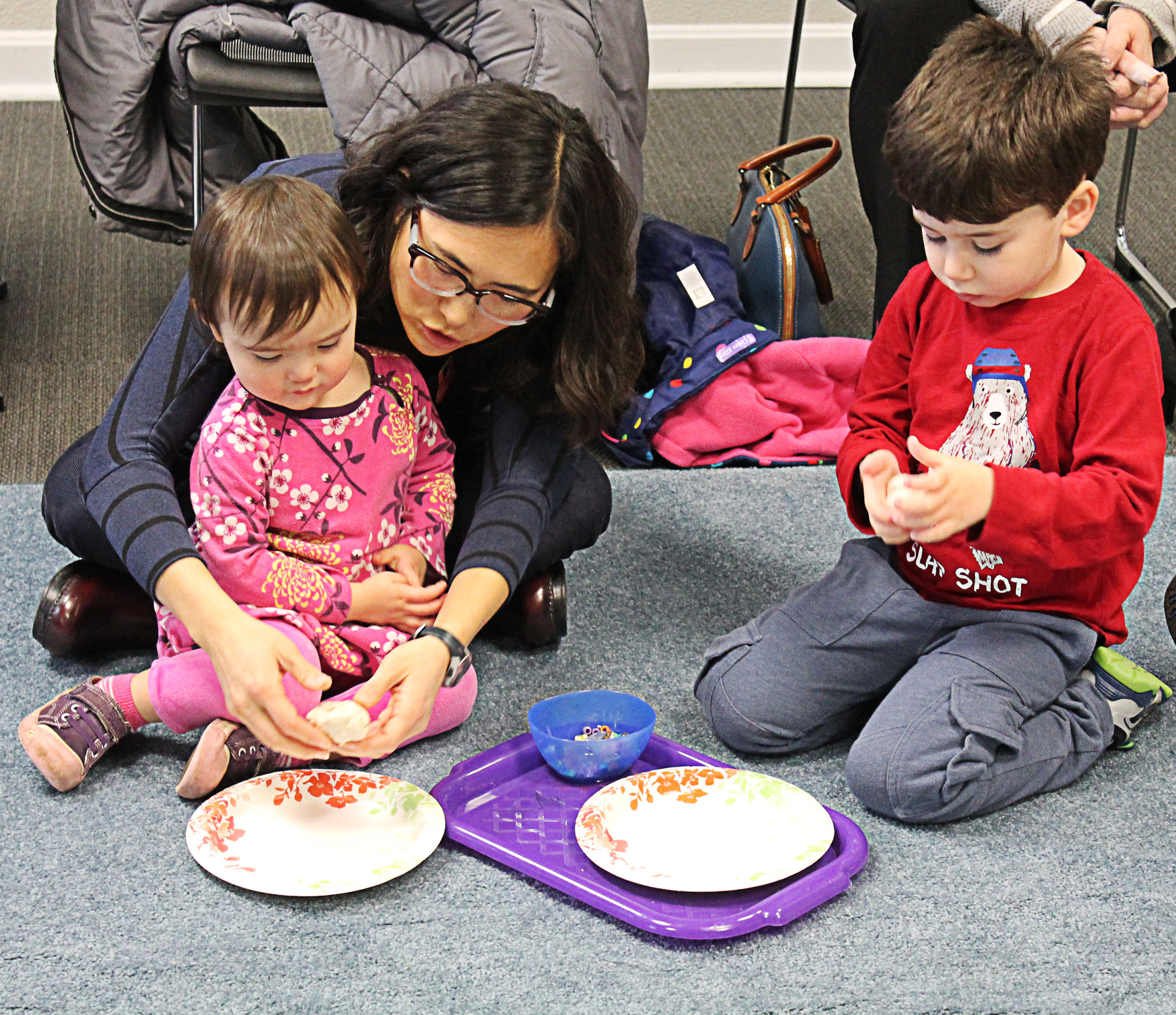 a parent with her preschool child and another preschool child next to them work on an art project