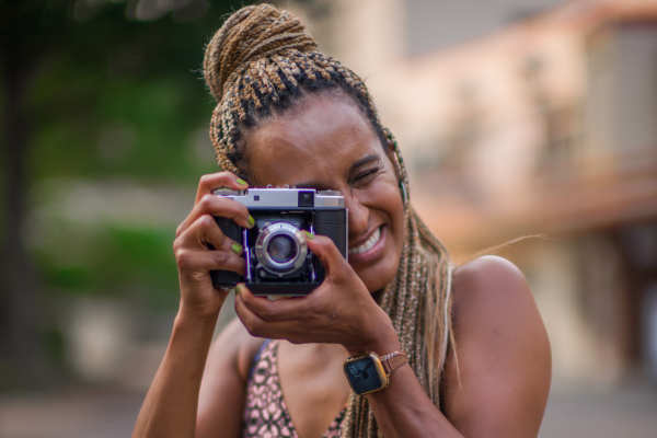 Close-up image of Redeat Wondemu. She is smiling and holding a film camera in front of her face, looking into the viewfinder of the camera.