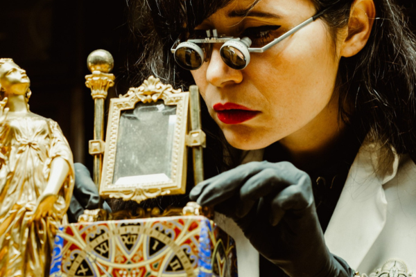 Image of Brittany Nico Cox working on an ornate clock. The image is close up, and she is wearing magnifying glasses.