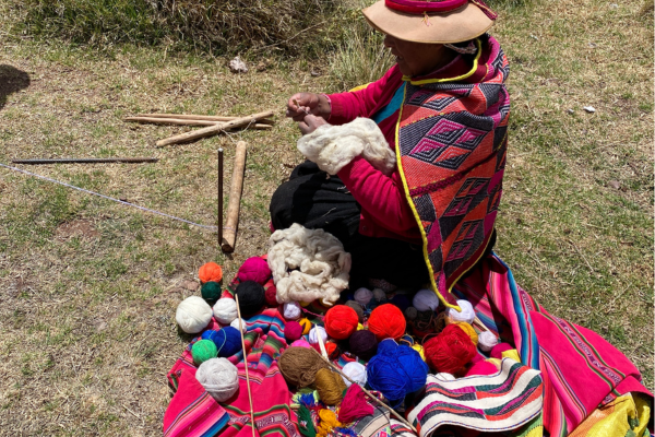 Image of a Peruvian woman weaving a colorful textile while sitting outdoors.