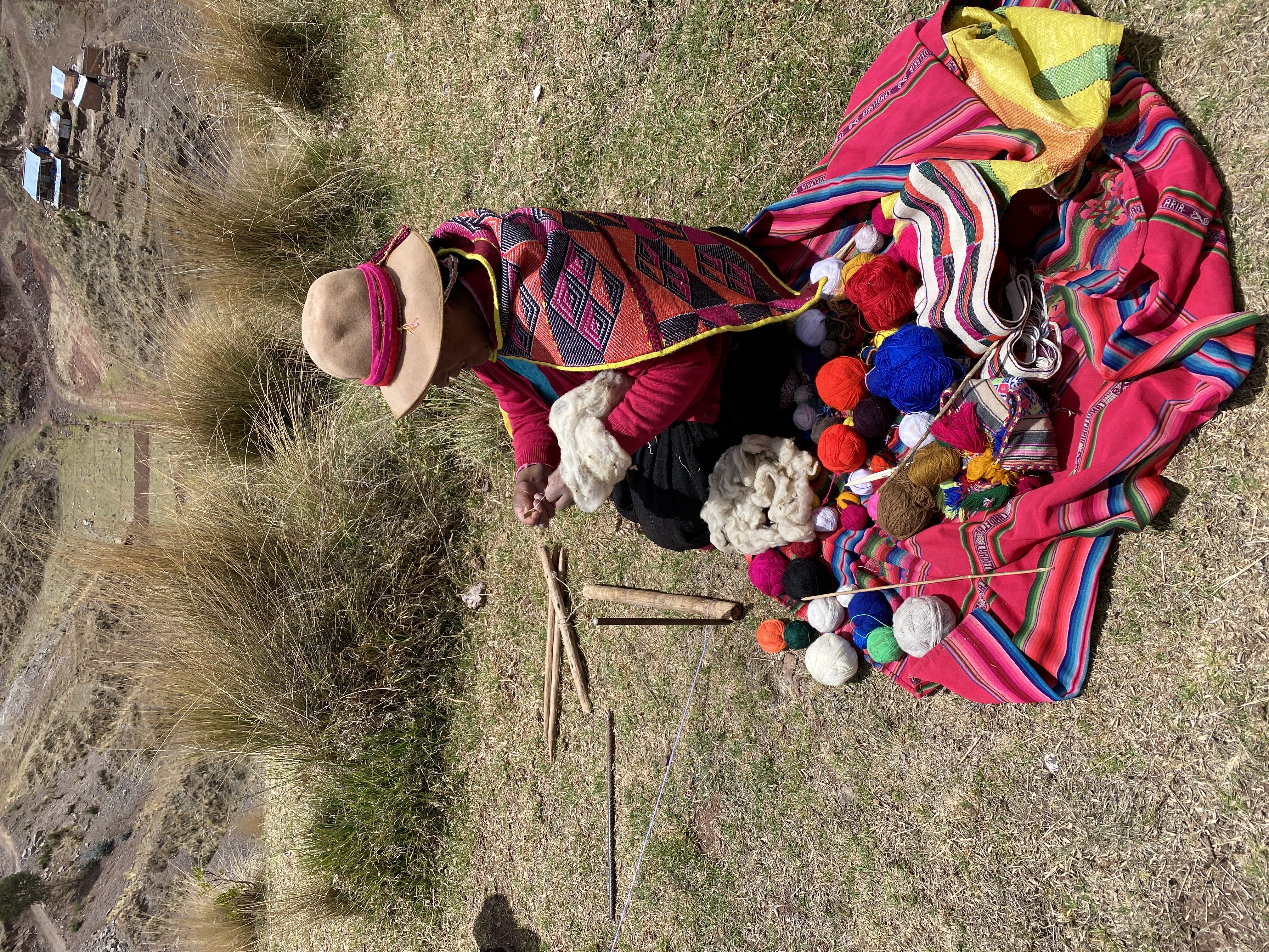 Image of a Peruvian woman weaving a colorful textile outdoors.