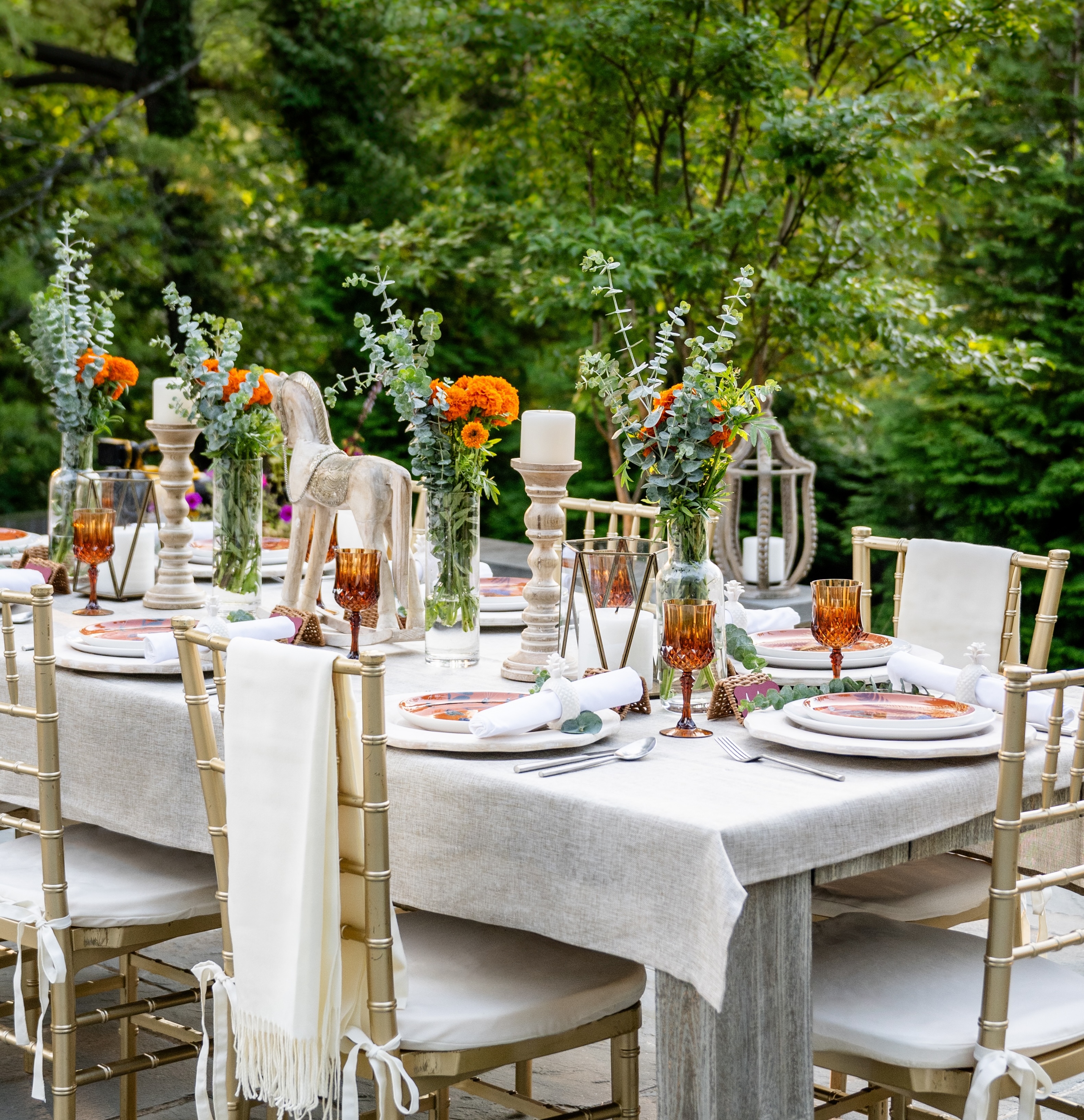 Image of a beautifully decorated table scape on an outdoor table, surrounded by lush green trees.