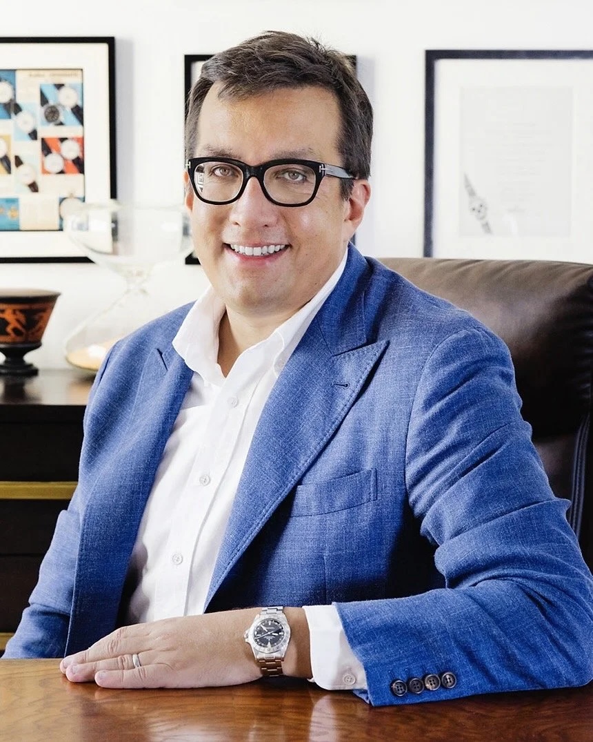 Headshot of Eric Wind, who is wearing a blue suit and posing with a wristwatch.