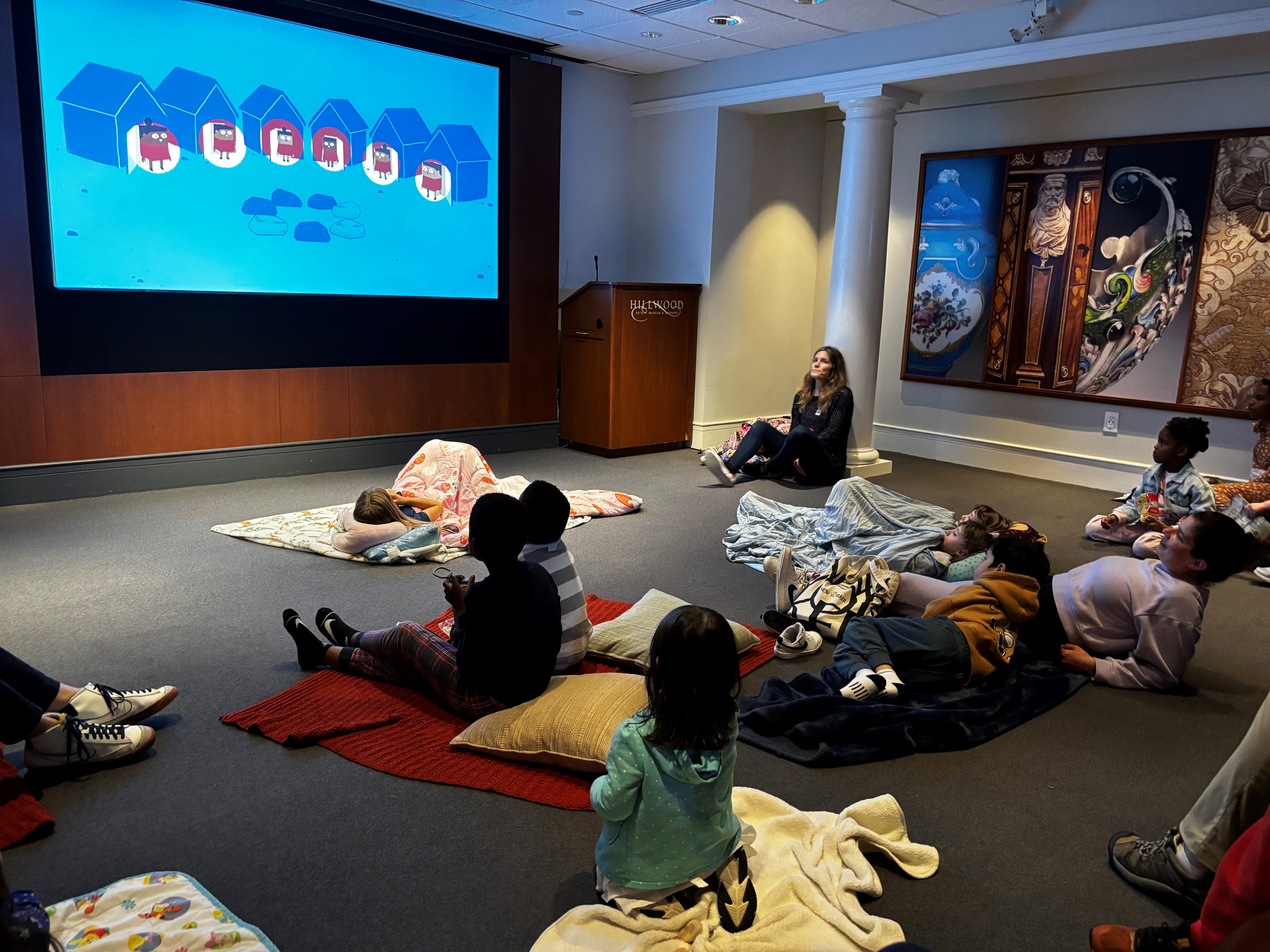 Children lying on floor with blankets and pillows watching an animated movie.