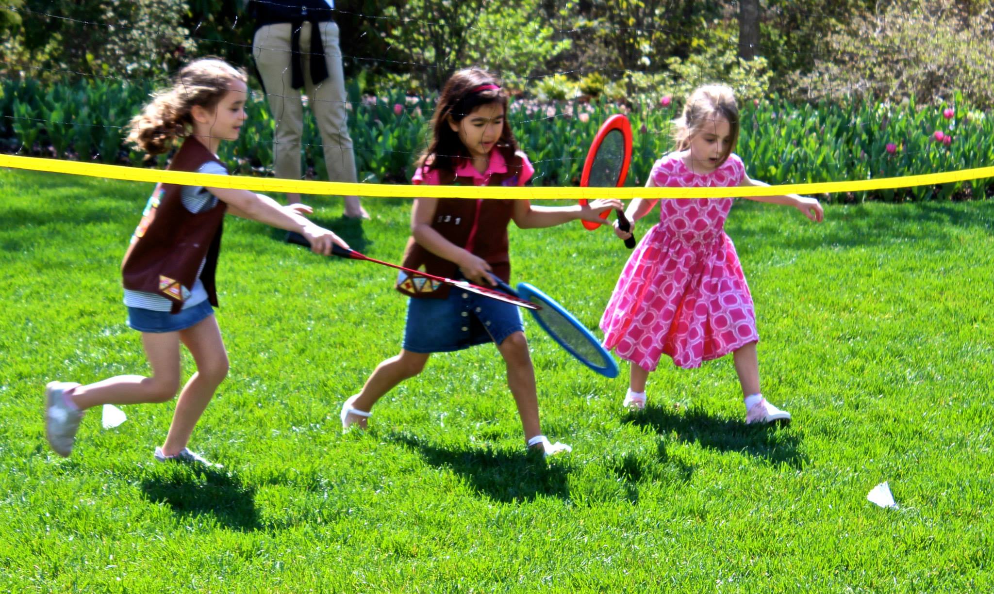 Three girls playing badminton on the lawn.