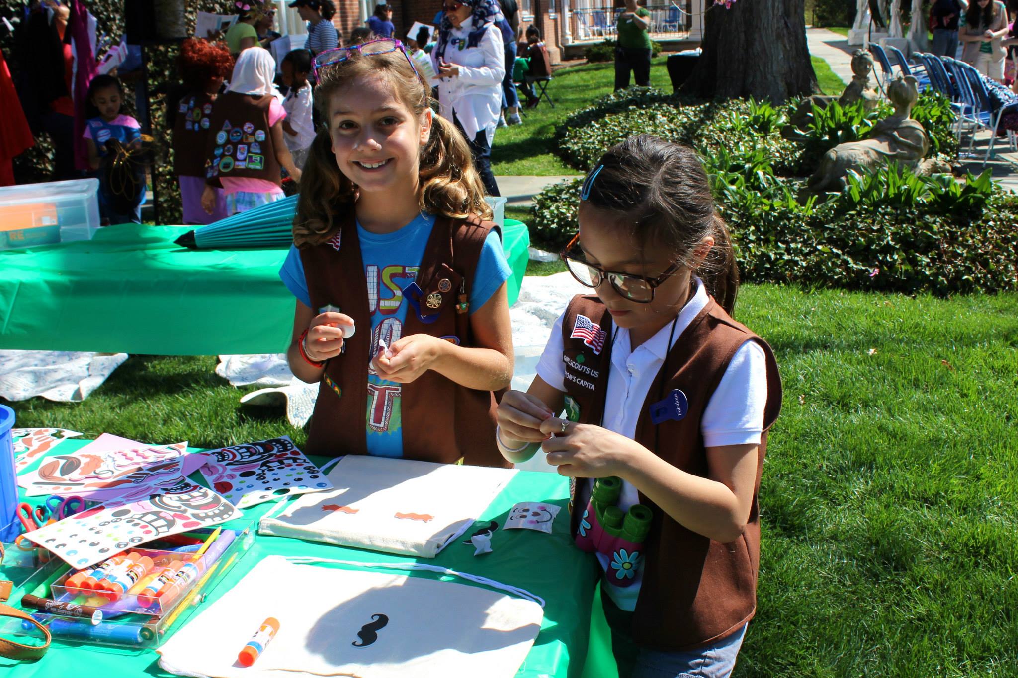 Two Brownie Girl Scouts smiling and working on an art project in Hillwood's gardens.