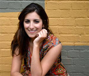 Lena Seikaly sits in front of a bright yellow wall 