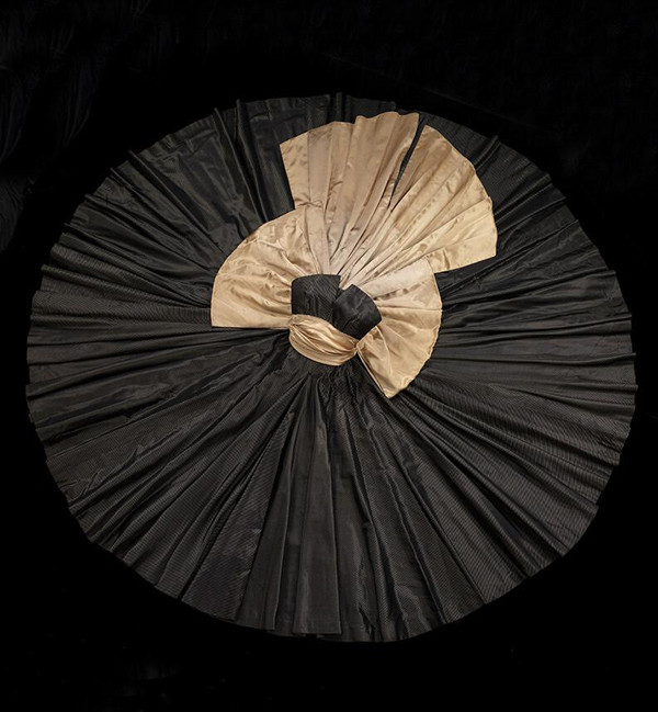 Strapless black Christian Dior dress laid out in a circle, accented with champagne colored sash and bow