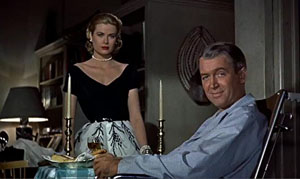 Grace Kelly in a beautiful evening gown visits James Stuart's apartment. Stuart is wearing pajamas and sitting in a wheelchair due to a leg injury.