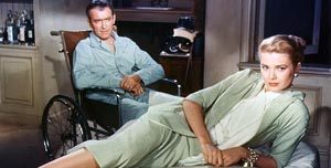 Grace Kelly lies on her side in a bed, wearing a key-lime colored skirt suit, while James Stuart wears pajamas and sits in a wheelchair due to a leg injury