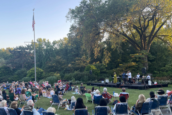 Image of visitors gathered on a grassy lawn to watch a jazz concert.