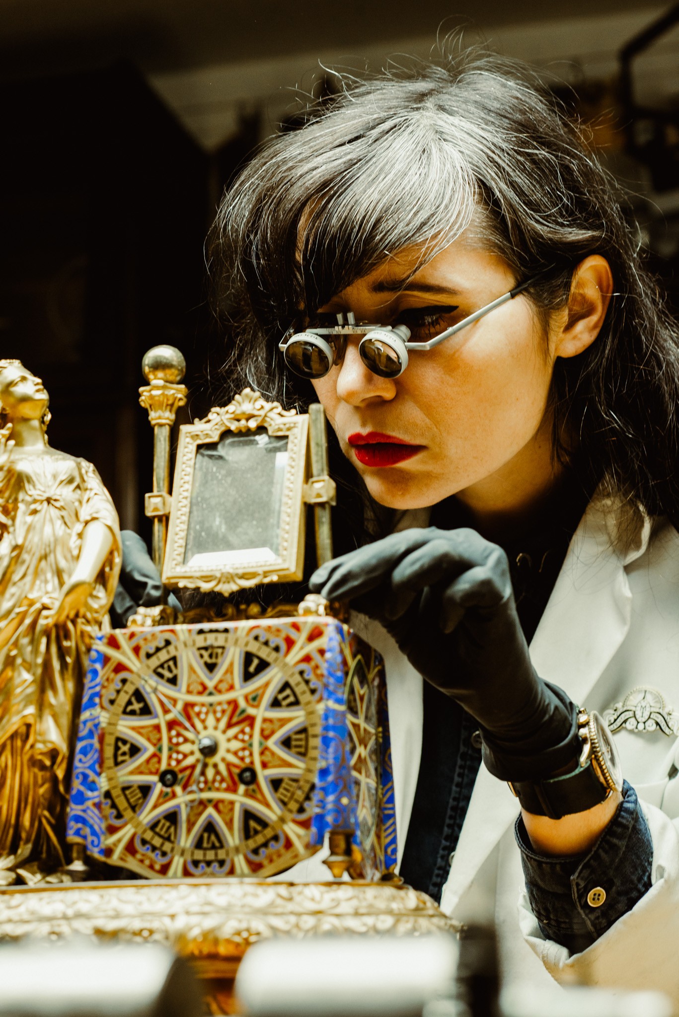 Close -up image of Brittany Cox working on an ornate clock. She is wearing magnifying glasses.