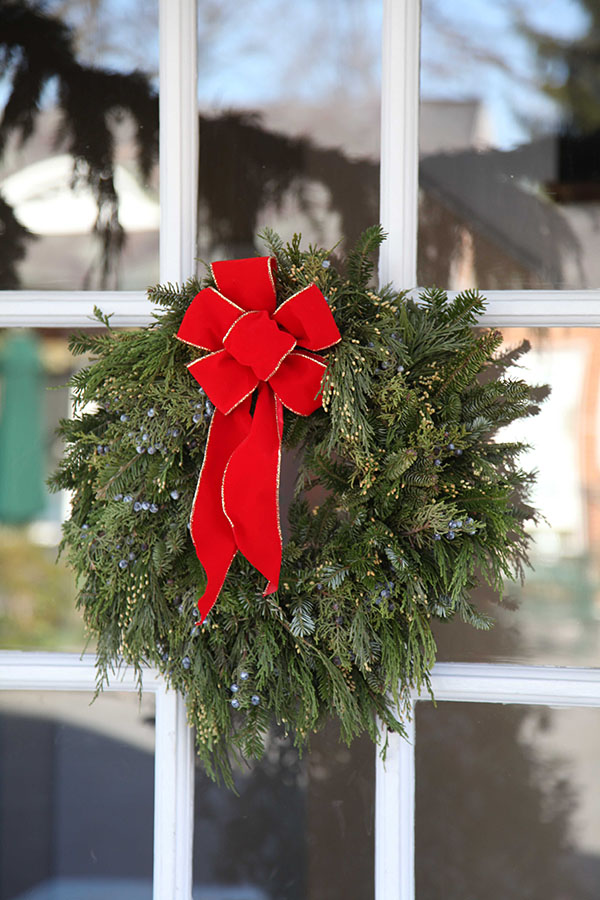 Evergreen wreath with red bow hung at Hillwood on a door with window