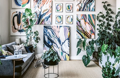 Living room with sofa, white walls, bold, colorful abstract prints, and masses of houseplants