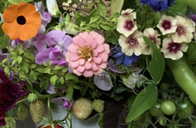 Summery floral arrangement including brightly colored small blooms and summer fruits lincluding strawberries and peas.