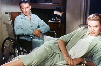 Grace Kelly lies on her side in a key-lime green suit while James Stuart sits behind her in a wheelchair wearing pajamas
