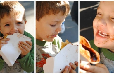 Young child with short brown hair, eating crepes and smiling