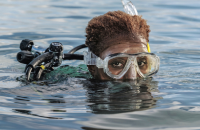 Image of Tara Roberts, a diver, emerging from the water, with just the top half of her face and goggles visible.