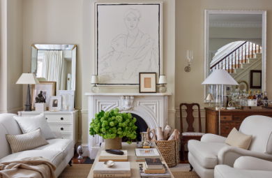 Image from the cover of "Artful Home" by Josh Young. The image features a large pencil-line portrait hanging over a white fireplace. There are white couches on the periphery of the image, with a light wooden coffee table between the couches. The coffee table features a fluffy, green house plant.