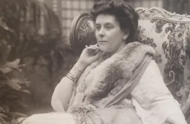 Image of a photographic portrait of Olga Paley. She sits in a chair with her head resting on her hand. 