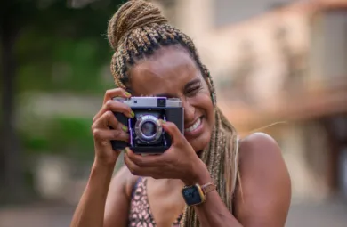 Close-up image of Redeat Wondemu. She is smiling and holding a film camera in front of her face, looking into the viewfinder of the camera.
