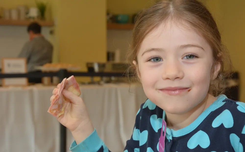Young girl with light brown hair smiling while holding crepe in right hand