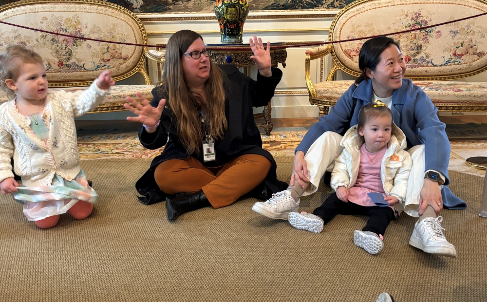 a teacher, preschool students, and a parent, gesture and point excitedly at art in the mansion