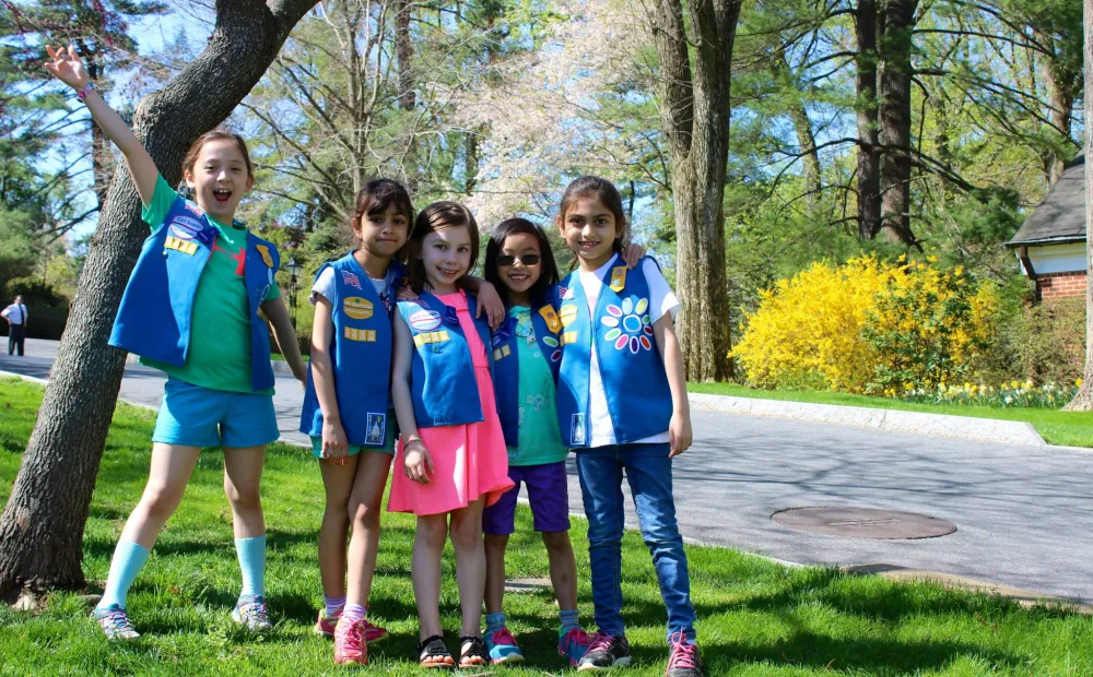 Five Daisy Girl Scouts gathered together and smiling outdoors in Hillwood's gardens