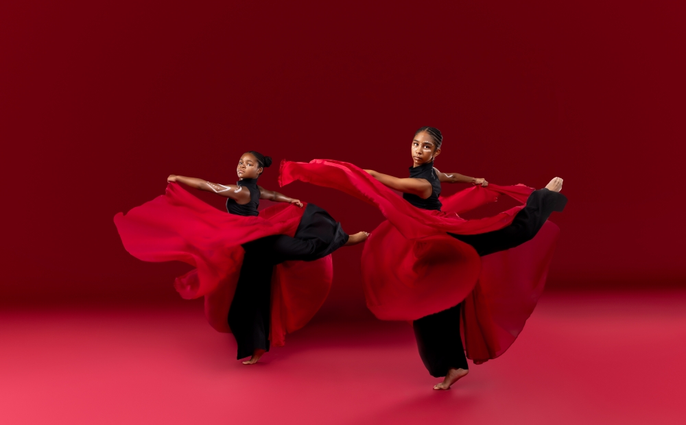 Image of two young dancers with red scarves wrapped around them. 