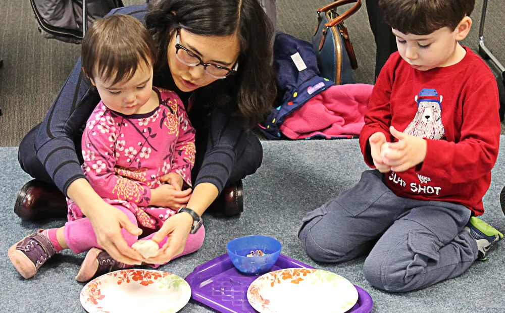 a parent with her preschool child and another preschool child next to them work on an art project